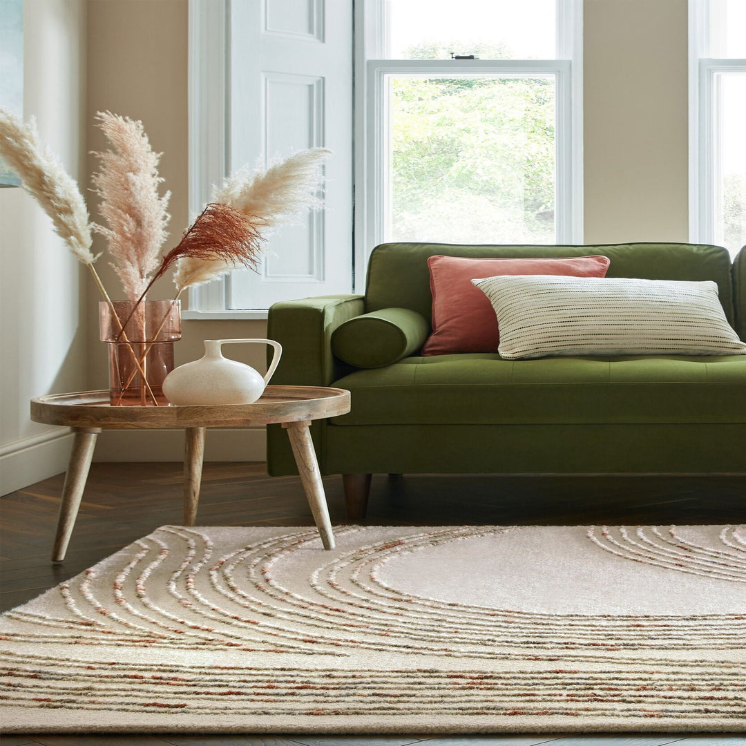 le tapis en lain sworl coloris orange et naturel est présenté dans un salon devant un canapé vert#couleur_naturel-orange