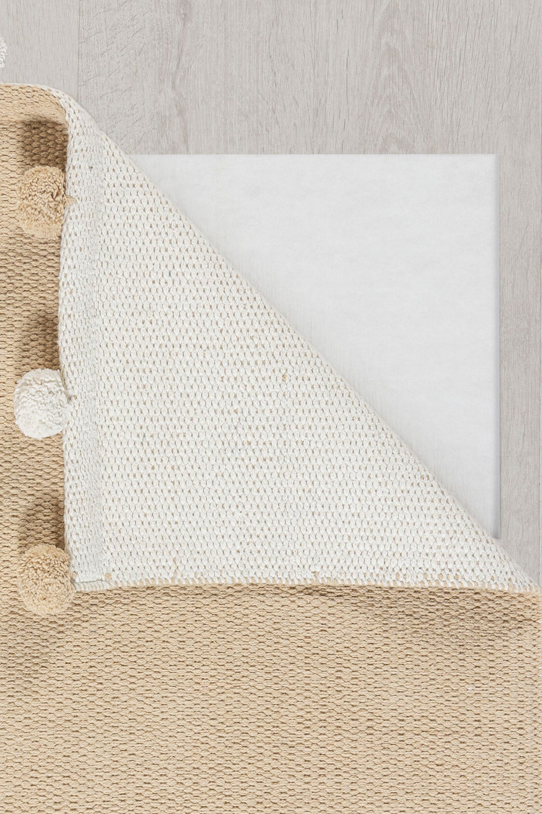 image montrant un angle du tapis pompom beige replié afin de voir l'envers du tapis de coloris blanc#couleur_naturel